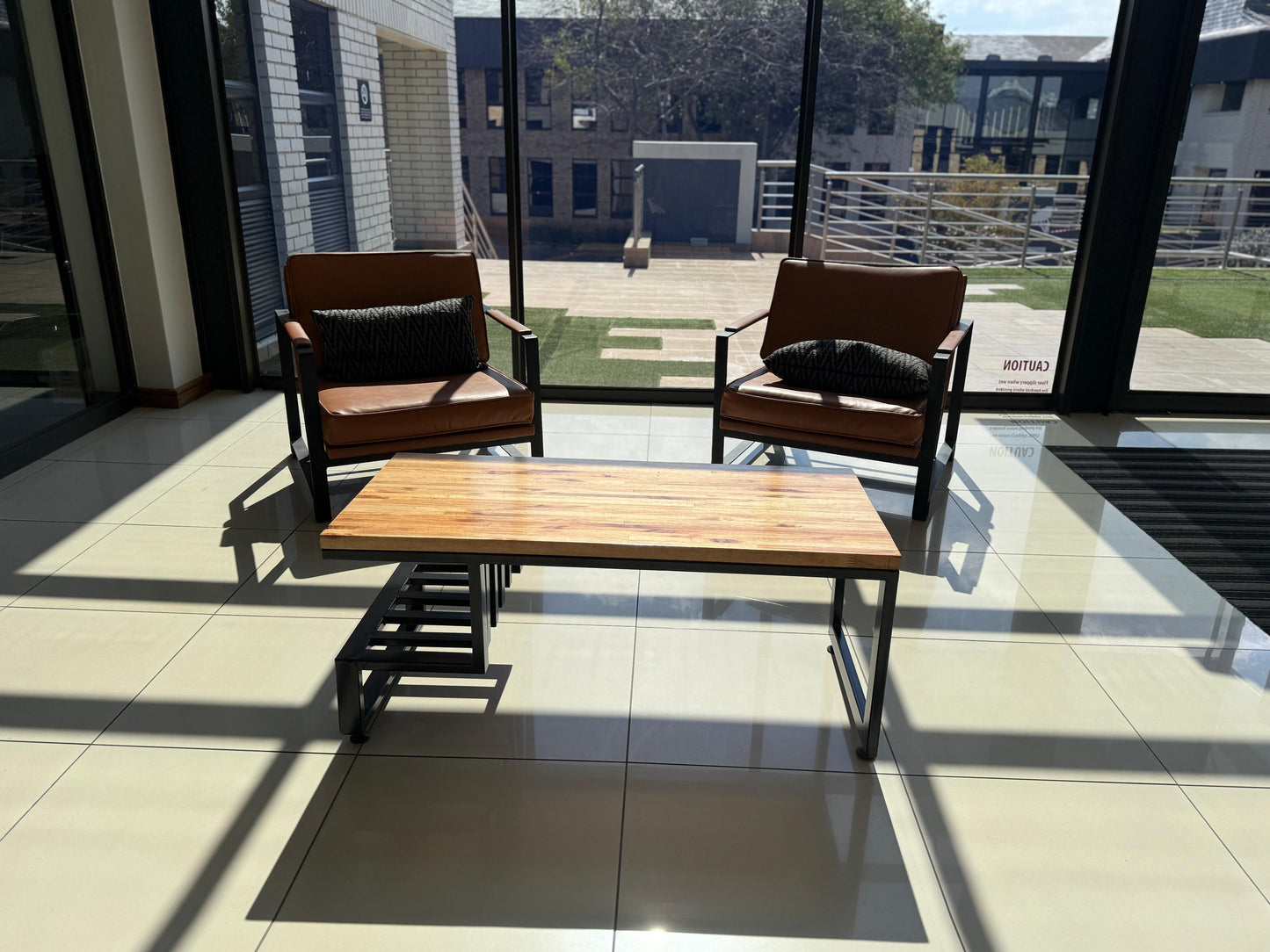 Two brown chairs with black cushions and a wooden coffee  table in a modern indoor setting with large windows.